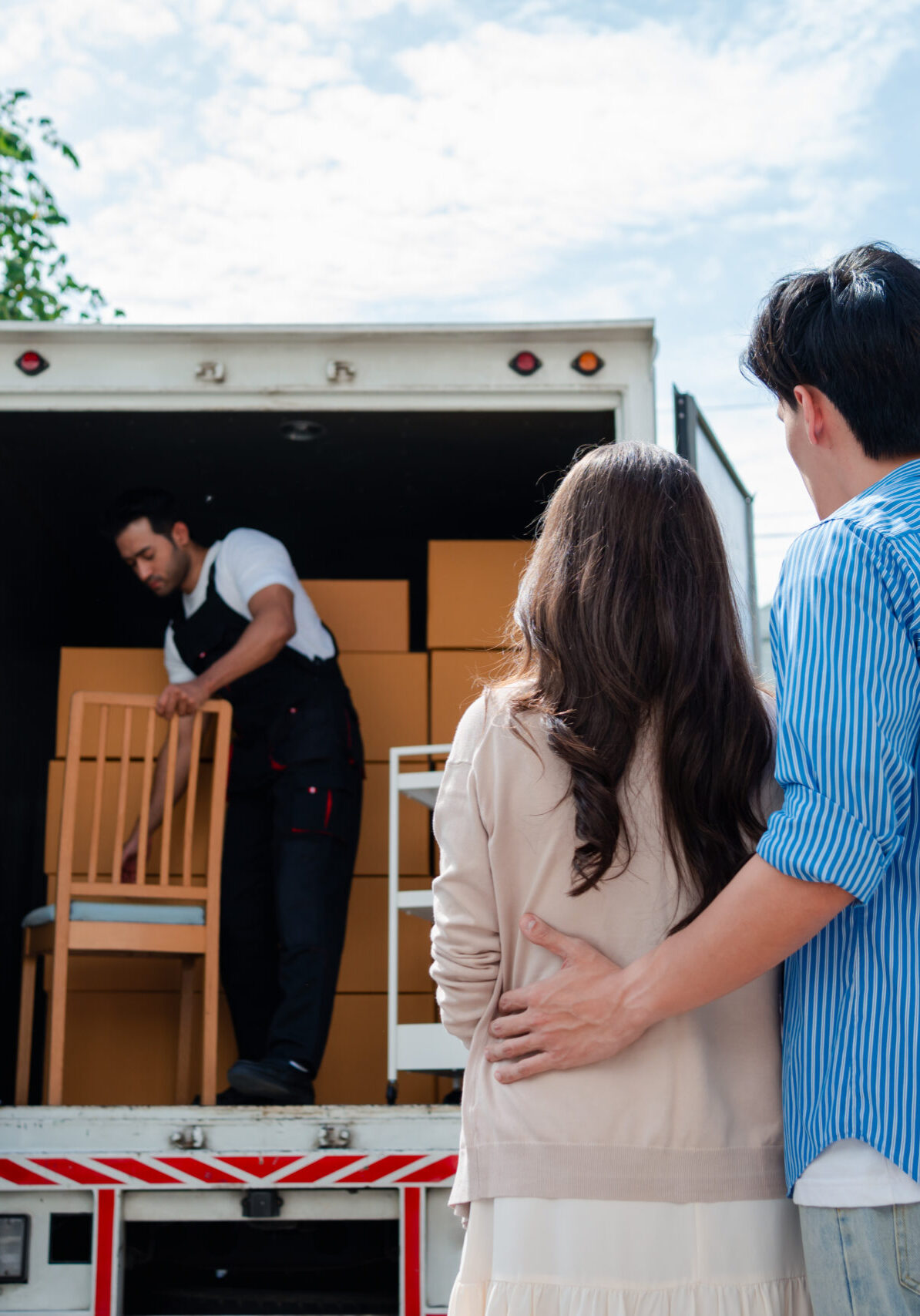 Asian Couple check while unloading boxes and furniture from a pickup truck to a new house with service cargo two men movers worker in uniform lifting boxes. concept of Home moving and delivery.
